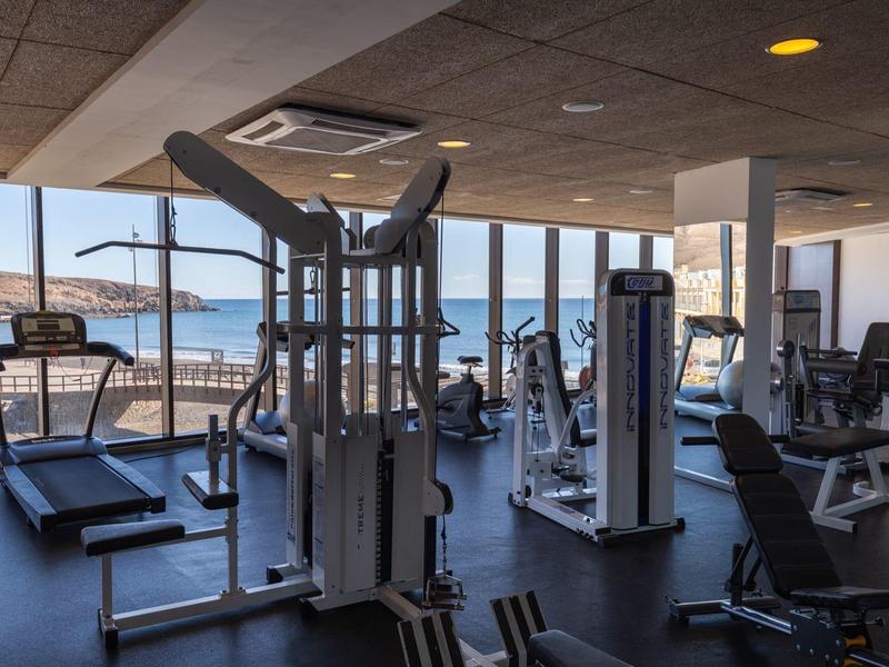 Moderne sportschool met diverse fitnessapparatuur en grote ramen met uitzicht op zee.