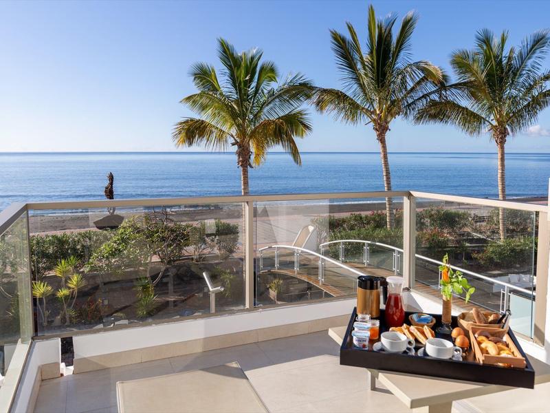 Balkon met ontbijtplank met uitzicht op palmbomen en oceaan op een zonnige dag.