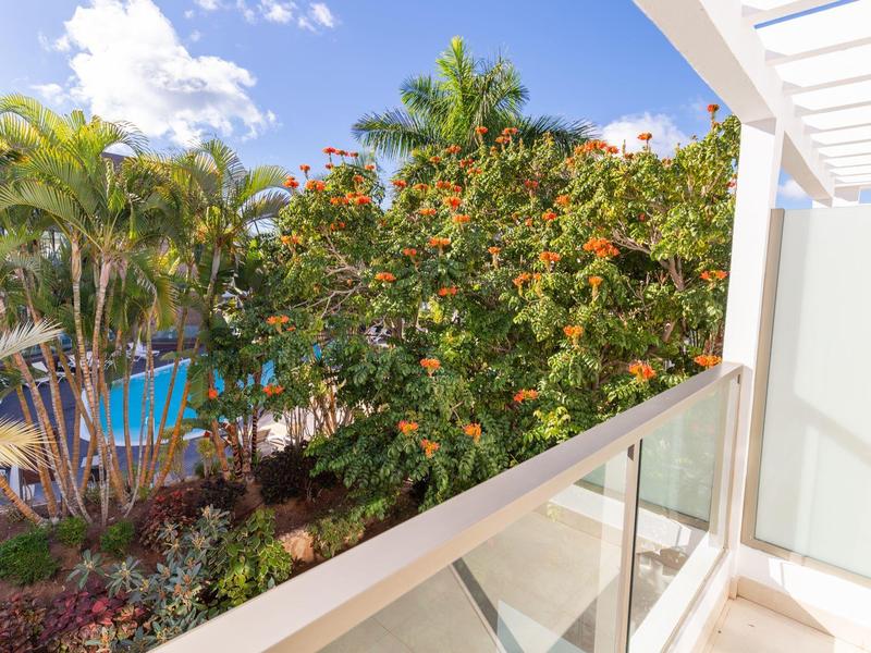 Balkonuitzicht op weelderig groen en een deels bewolkte blauwe lucht.