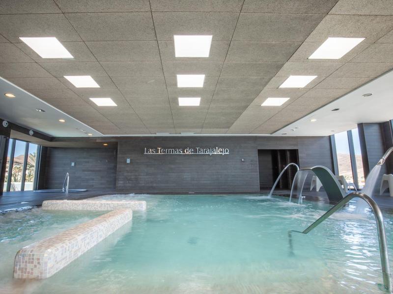 Binnenzwembad in hotel met helder water, jets en moderne verlichting in grijze tegelplafond.