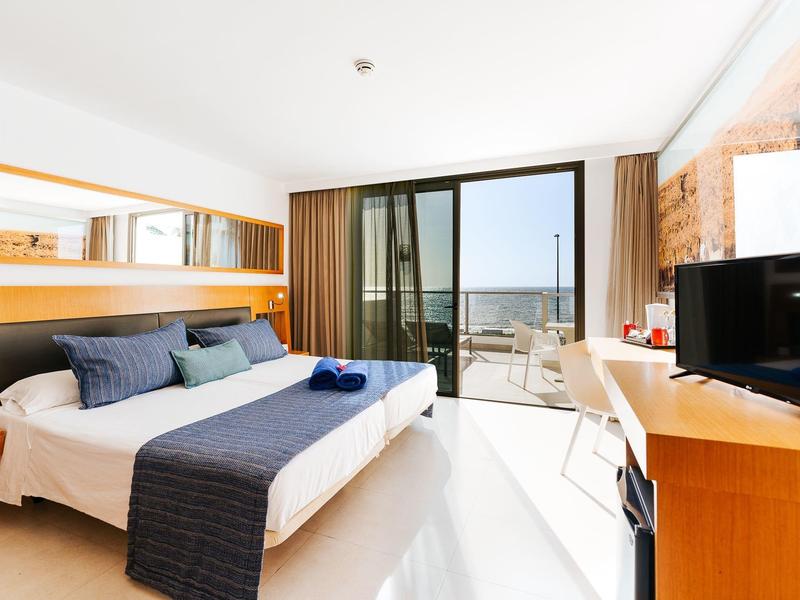 Moderne hotelkamer met groot bed, balkon en zeezicht bij daglicht.