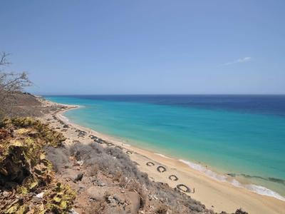 Costa con agua turquesa, playa arenosa y ladera rocosa bajo cielo despejado.