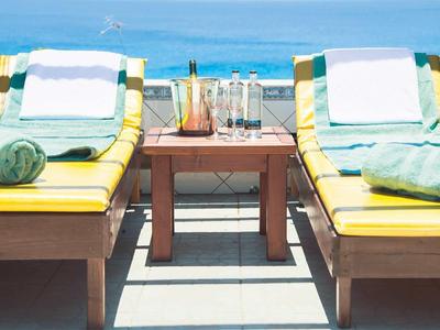 Dos tumbonas amarillas con toallas verdes y bebidas en una terraza de madera con vista al mar.