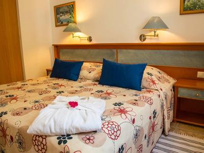 Gemütliches Schlafzimmer mit Doppelbett, blauen Kissen, Blumendecke und Nachttisch mit Lampe.