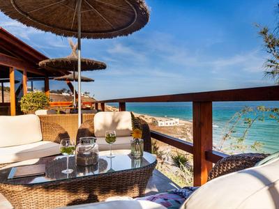 Terraza acogedora con muebles de mimbre y vista al mar en un día soleado.
