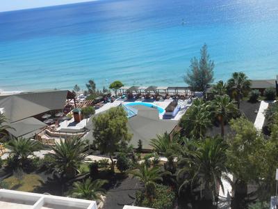 Vista de una piscina de hotel con tumbonas y vista al mar azul y la playa en el fondo.