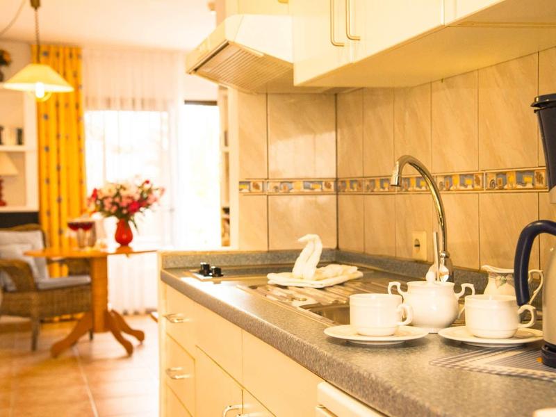 Cocina luminosa con cafetera y tazas de té, área de comedor acogedora al fondo.