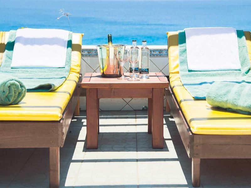 Dos tumbonas amarillas con toallas verdes y bebidas en una terraza de madera con vista al mar.