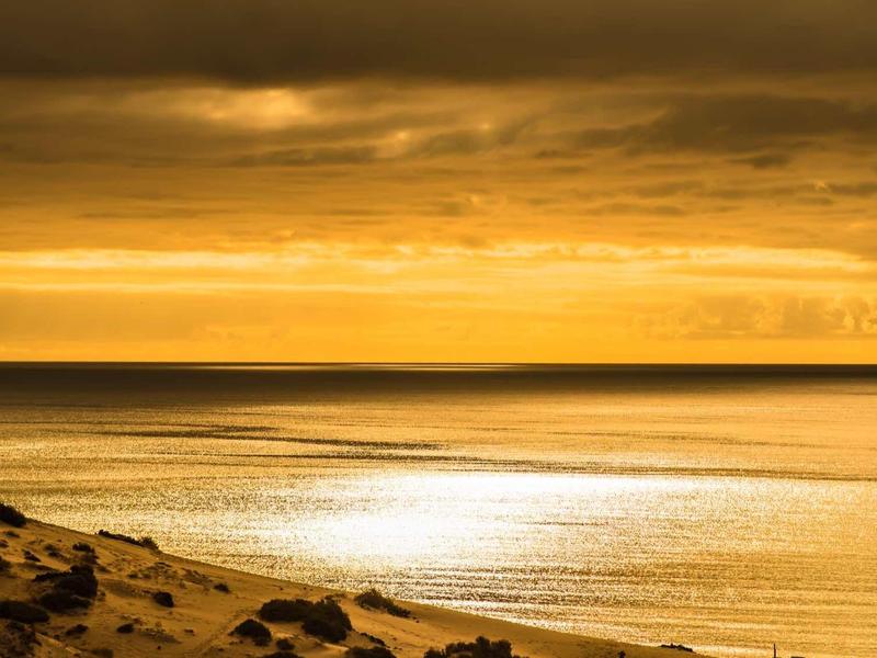Ambiente de atardecer dorado sobre mar tranquilo en playa rocosa.