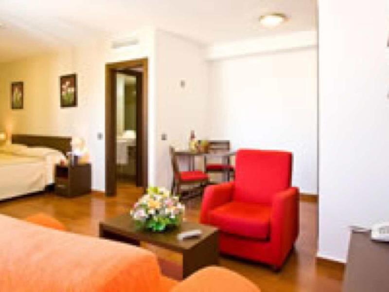 Bright hotel room with a red armchair, table, double bed, and sitting area.