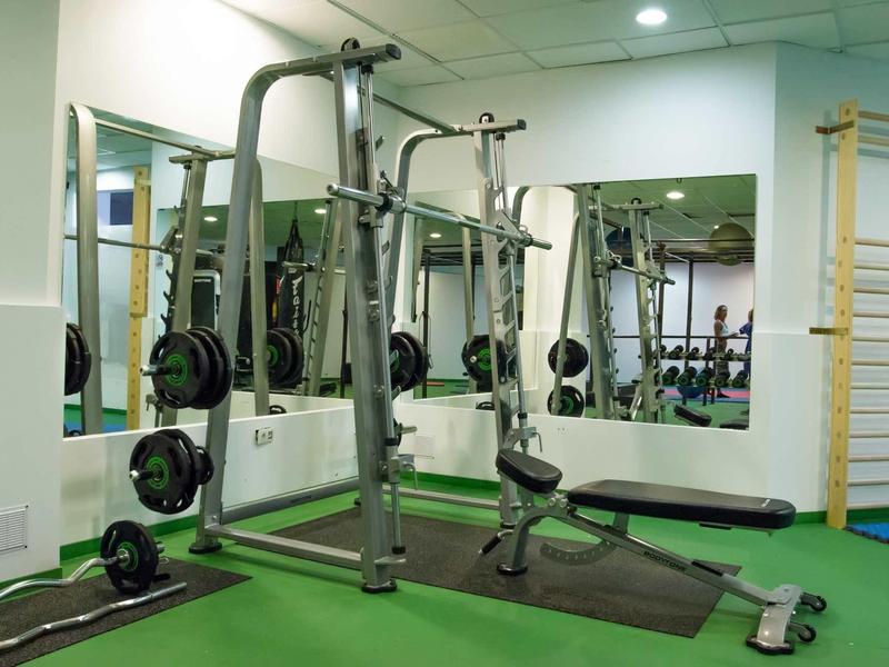 Small gym with strength training equipment and mirrors on the walls.