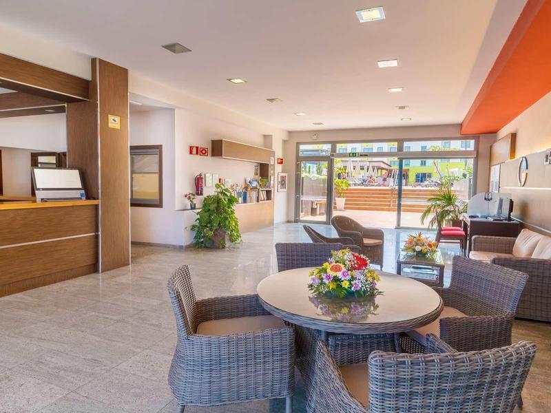 Modern hotel lobby with reception desk, seating area, and large windows letting in daylight.