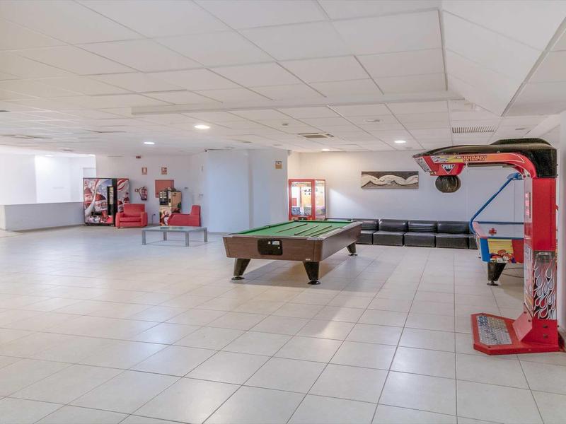 Large recreation room with pool table, basketball game, and table tennis on bright white tiles.