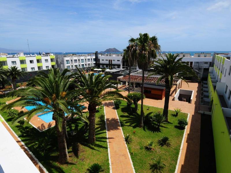 View of a hotel courtyard with pool, palm trees, and clear blue sky.