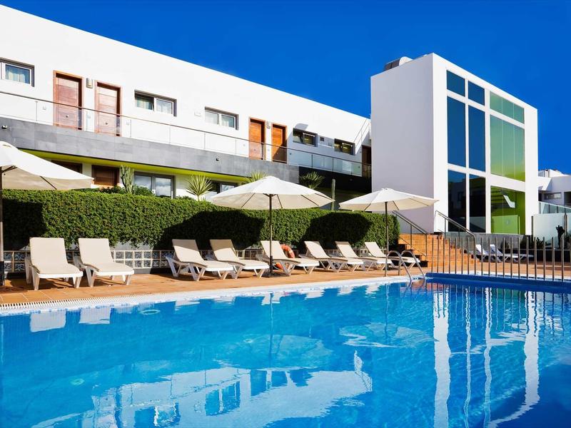 Modern hotel pool area with lounge chairs and umbrellas in front of a white building.