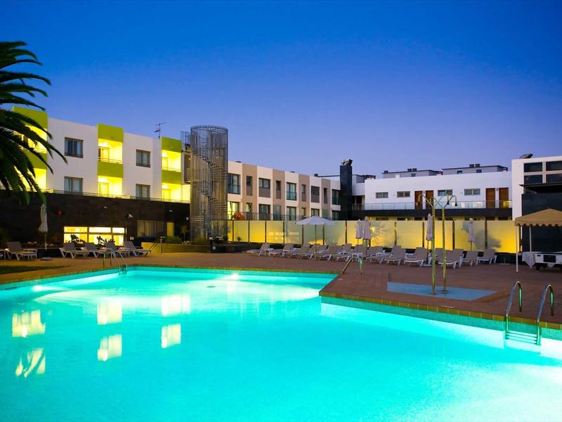 Modern hotel with illuminated outdoor pool and lounge chairs in the evening