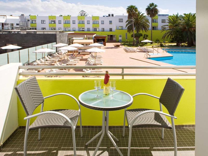 Balcony with table, two chairs, and hotel pool area with sun loungers.