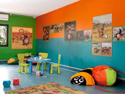 Bunter Kinderspielraum mit bunten Wänden, kleinen Tischen, Stühlen, Würfeln und einem Marienkäfer-Kissen.
