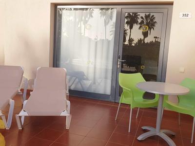 Balkon mit zwei weißen Liegestühlen und einem grauen Tisch mit zwei grünen Stühlen vor Glastür.