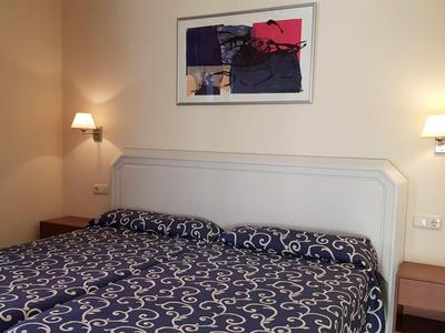 Ein helles Schlafzimmer mit einem Doppelbett, blau gemusterten Bettdecken, Nachttischen und Wandlampen.