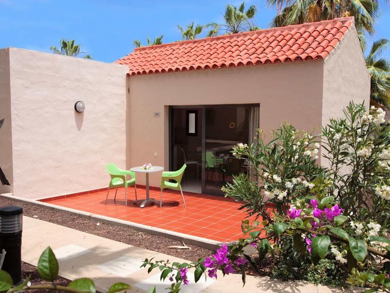 Terras met twee groene stoelen voor een wit gebouw met een rood dak en bloeiende planten.