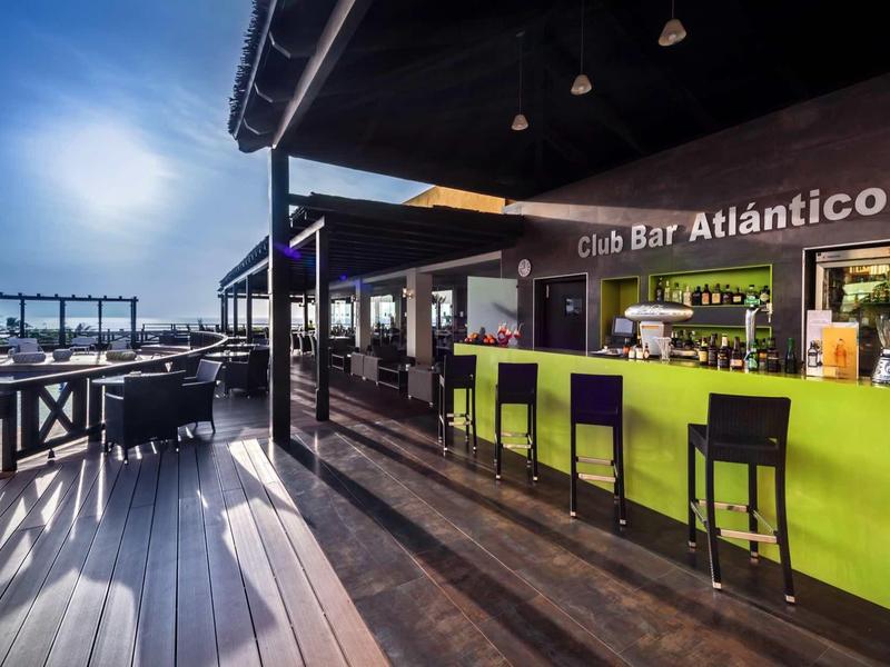 Moderner Außenbar mit grüner Theke, schwarzen Stühlen, Holzterrasse und Seeblick bei Abenddämmerung.