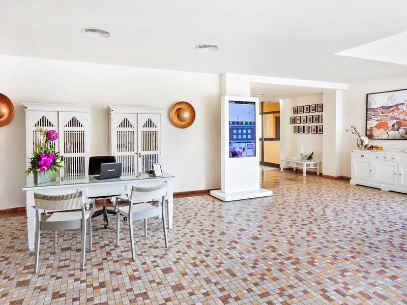 Hell eingerichteter Raum mit großem Tisch, weißen Stühlen, buntem Teppich und Kunst an den Wänden.