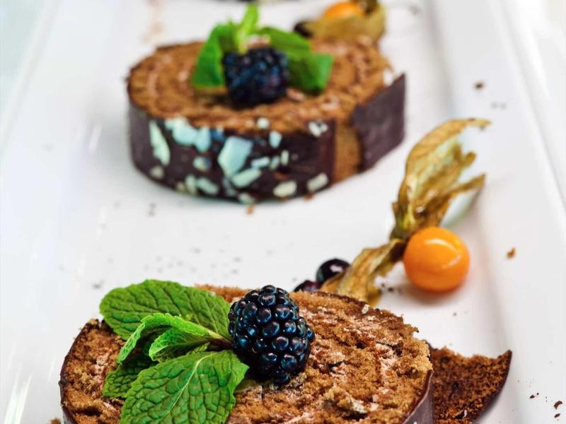 Drei runde Schokoladendesserts mit Minzblättern und Beeren auf weißem Teller.