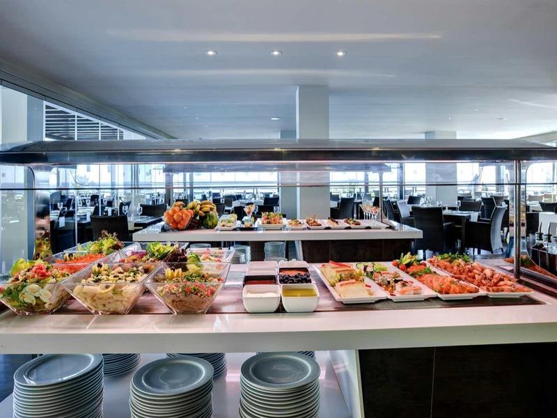 Buffet-Tisch mit verschiedenen Speisen in einem modernen, hellen Restaurant mit großem Fenster.