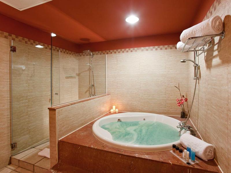 Modernes Badezimmer mit runder Wanne, Duschkabine, roten Deckenakzenten und warmem Licht.