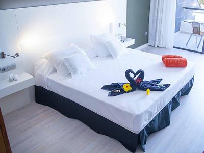 Hell eingerichtetes Schlafzimmer mit großem Bett, weißen Kissen und Handtüchern in Schwan-Form.