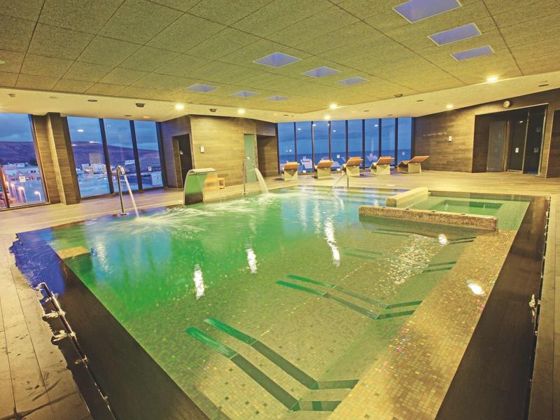 Verwarmd binnenzwembad met moderne verlichting en grote ramen met uitzicht op de stad.