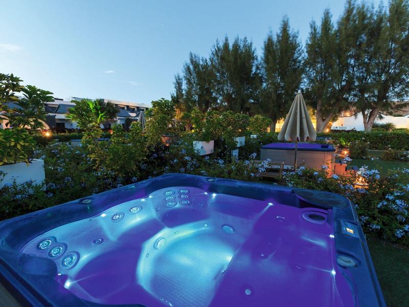 Verlicht bubbelbad in tuin met planten en avondlucht op de achtergrond.