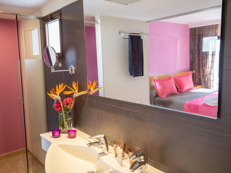 Moderne hotelkamer met roze bed, grote spiegel en nette badkamer met bloemen.
