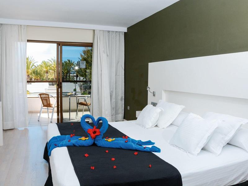 Modern hotelkamer met tweepersoonsbed, witte kussens, blauwe handdoeken en balkon met uitzicht op groen.