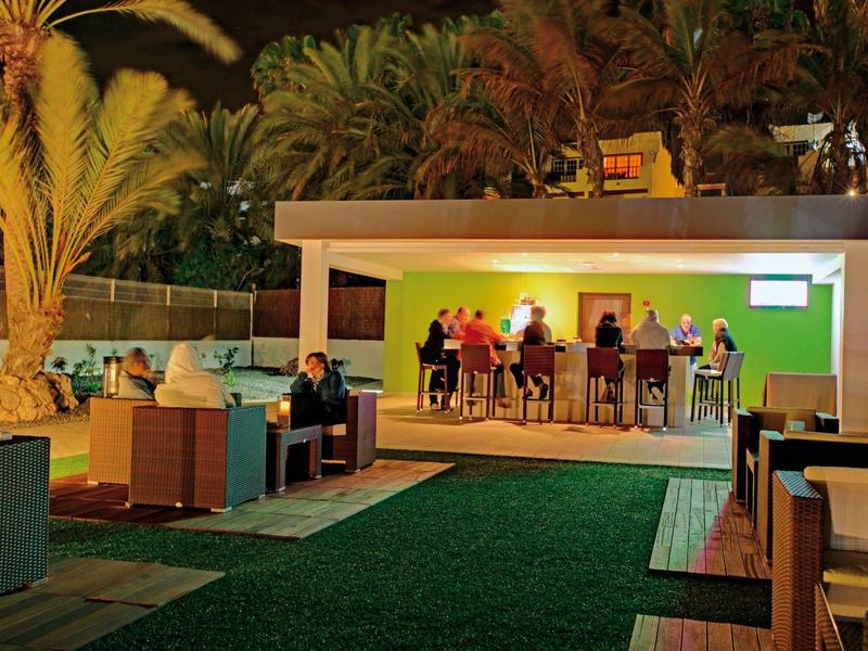 Buitenbar 's avonds met zitplaatsen en palmboomverlichting in een hotelomgeving.