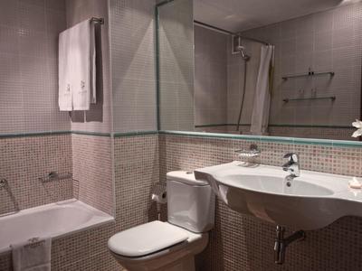 Kleines Badezimmer mit Badewanne, Toilette, Waschtisch und großen Spiegeln an den Wänden.