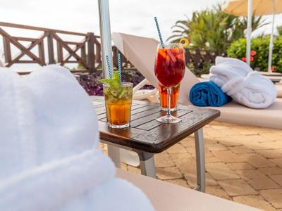 Due cocktail colorati e asciugamani su un tavolo tra lettini vicino alla piscina.