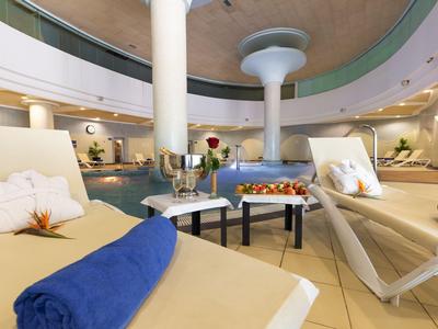 Elegante area piscina interna con comode sdraio, asciugamani blu e un tavolo con bevande e snack.