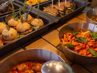 Varie pietanze calde e mini burger su un tavolo da buffet.