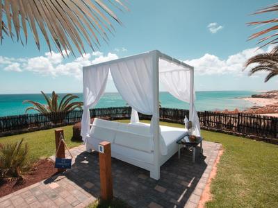 Lettino con baldacchino bianco e tende sulla spiaggia con vista mare e palme.