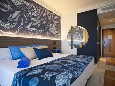 Modern hotel room with double bed, blue and white bedding, and decorative wall art.