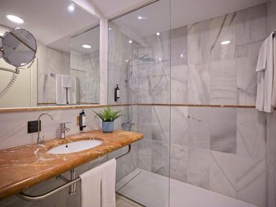 Bagno moderno con piastrelle in marmo, piano in legno e ampia doccia in vetro.