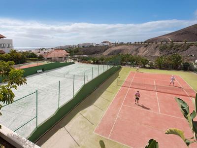 Two outdoor tennis courts, one red and one white, surrounded by hills.