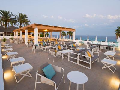 Grande terrasse d'hôtel avec espaces de sièges et vue sur la mer en pleine journée.