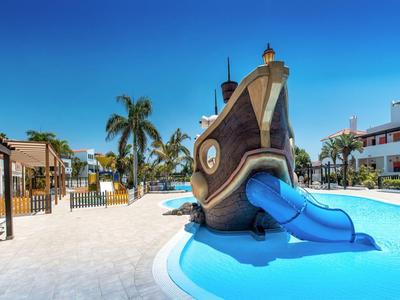 Water park with swimming pool and pirate ship slide under clear blue sky.