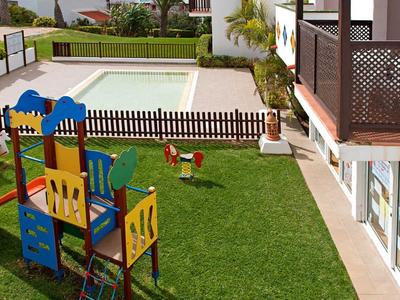 Playground with slide and swings next to a fenced pool on a hotel lawn.