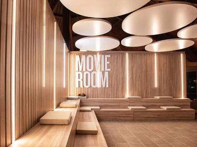 Modern movie room with wooden benches, soft lighting, and large white ceiling lights.