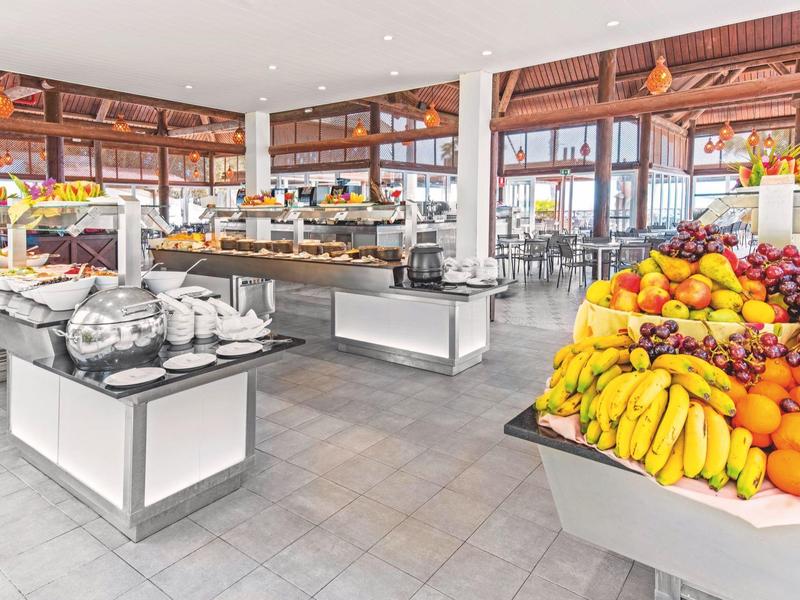 Buffet lumineux avec un large choix de fruits frais et des tables dressées dans une salle à manger moderne.