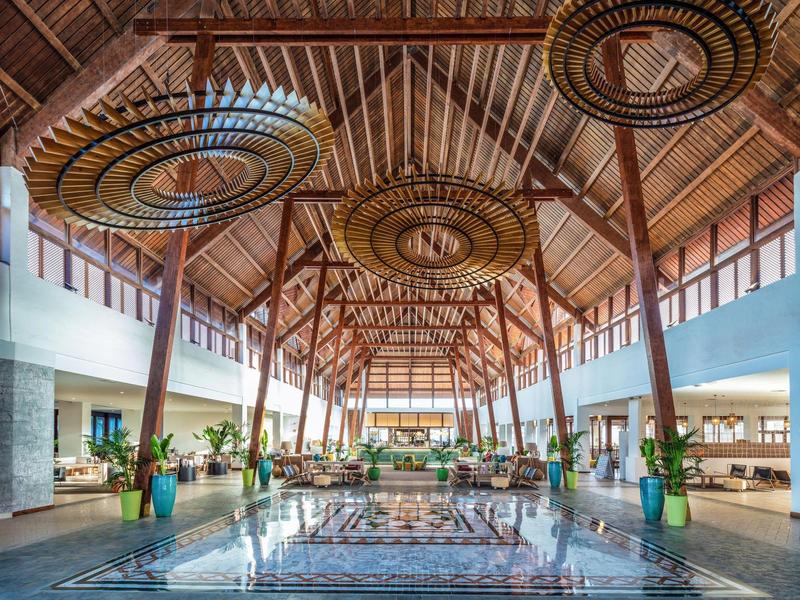 Grand hall d'hôtel avec hauts plafonds en bois, lustres modernes et aménagement ouvert.